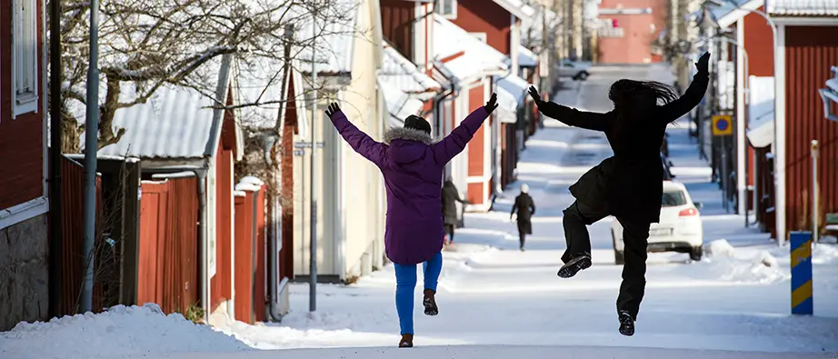 Två kvinnor gör glädjeskutt när de går på en snöig stadsgata.