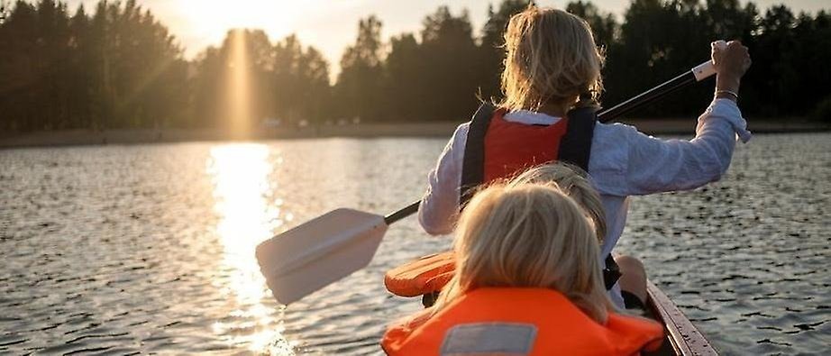 Vuxen och barn sitter i en kanot och paddlar i solnedgång